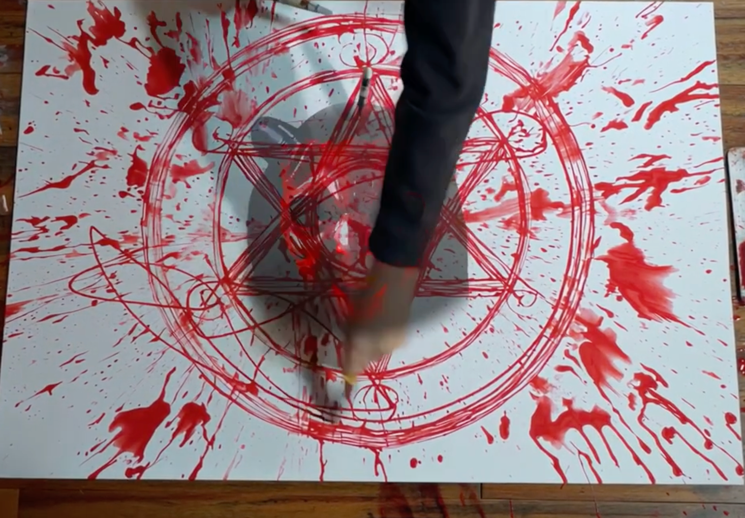 A Childs arm paints a star with a circle in red.  The center of the circle has demon face in it.